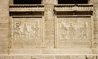 Zwei Reliefs, links ein Pharao, der Hathor und Horus ein Opfer darbringt, und rechts Hathor, die den jungen Ihy stillt, mit einem zweiten Ihy, der die weiße Krone von Oberägypten trägt